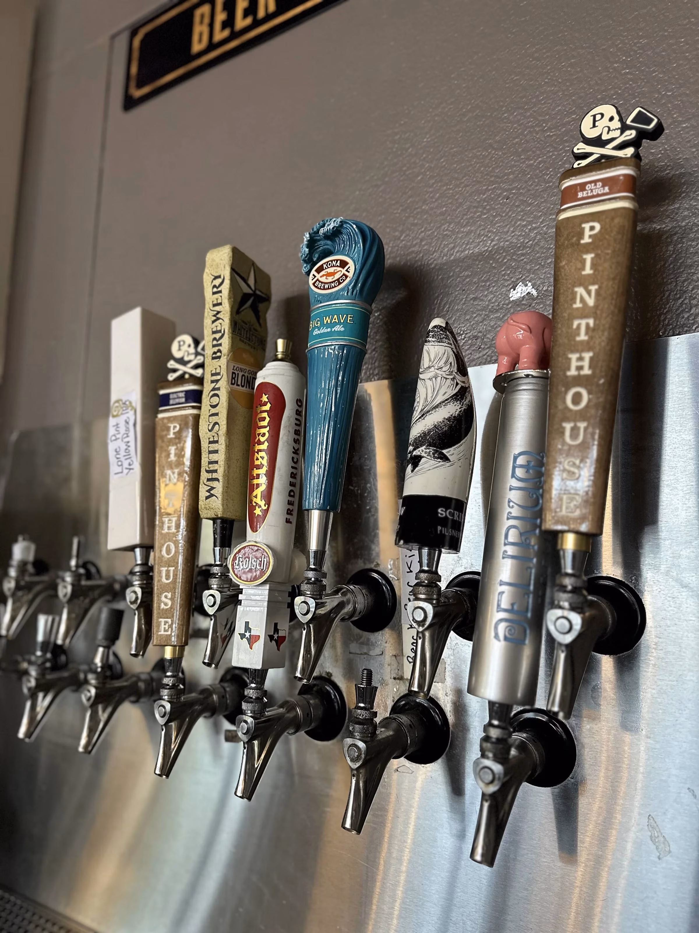 A row of various beer tap handles on a shiny metal surface.