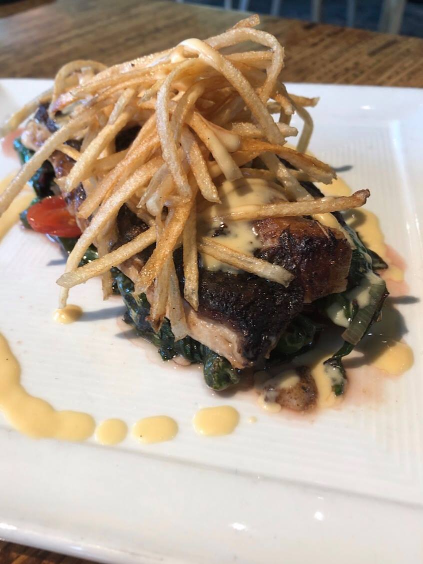 Seared fish, greens, shoestring fries, and creamy sauce on a white plate.