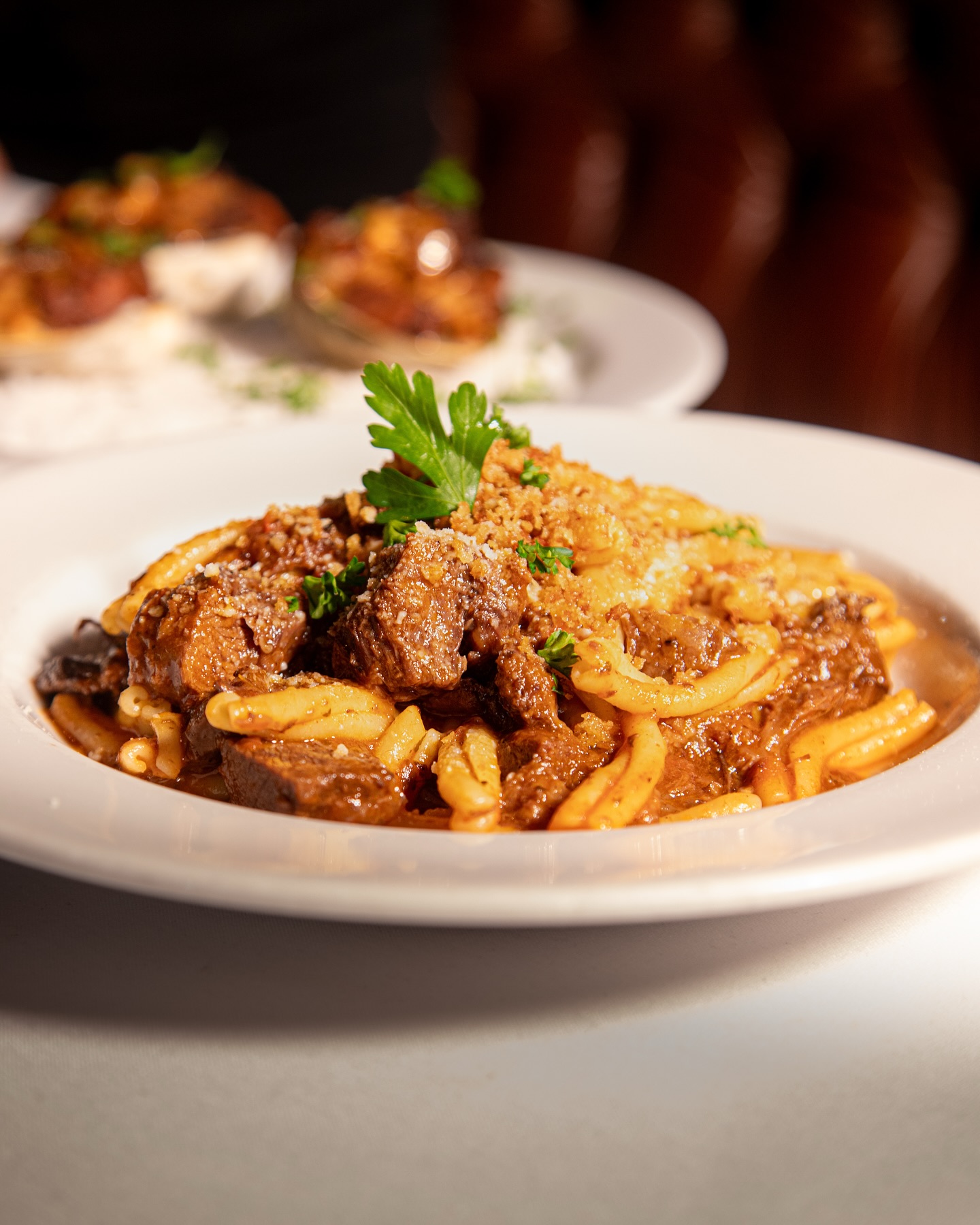 Pasta with stewed meat, sauce, granular topping, and parsley.
