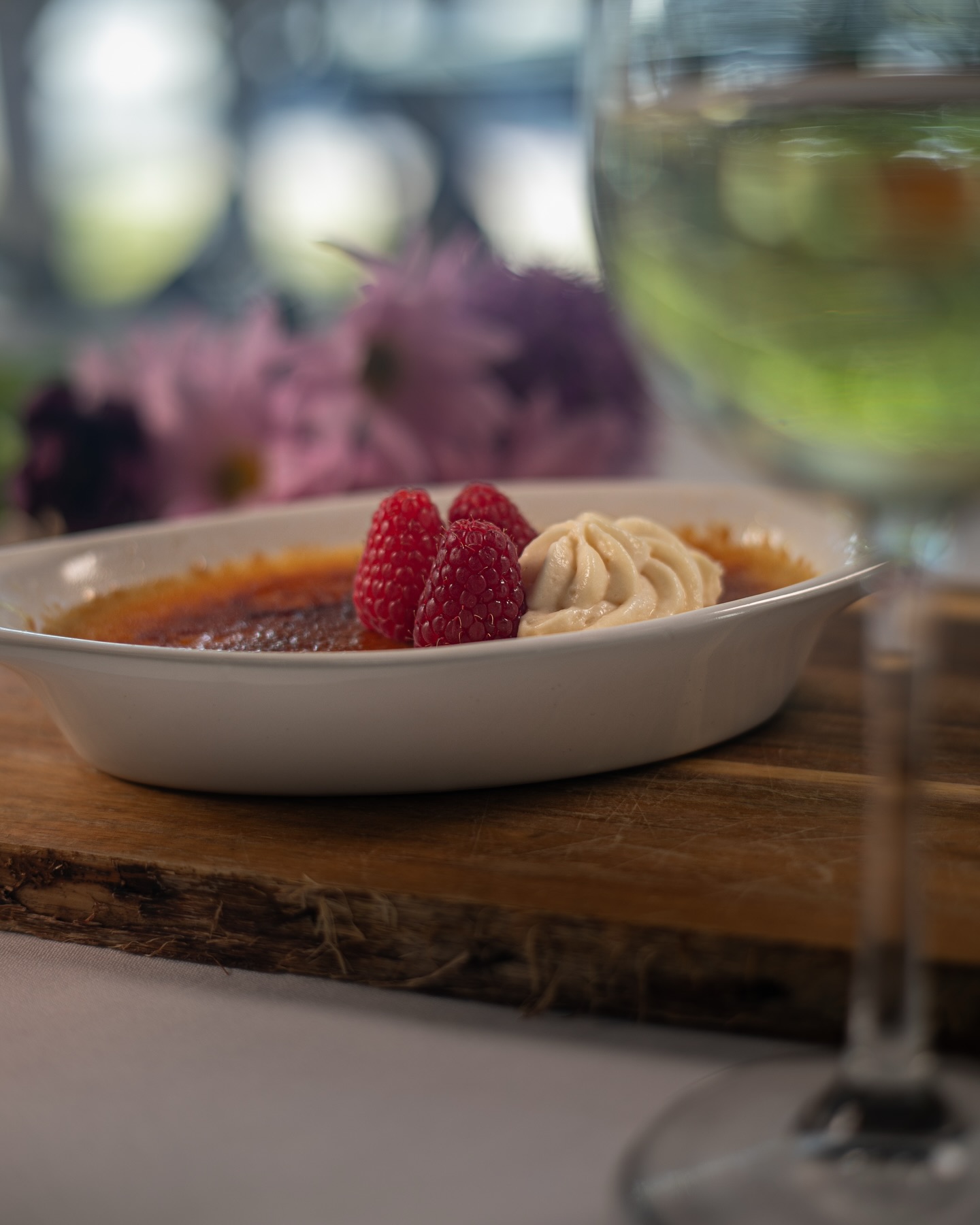 Crème brûlée with raspberries and cream on a wooden board.