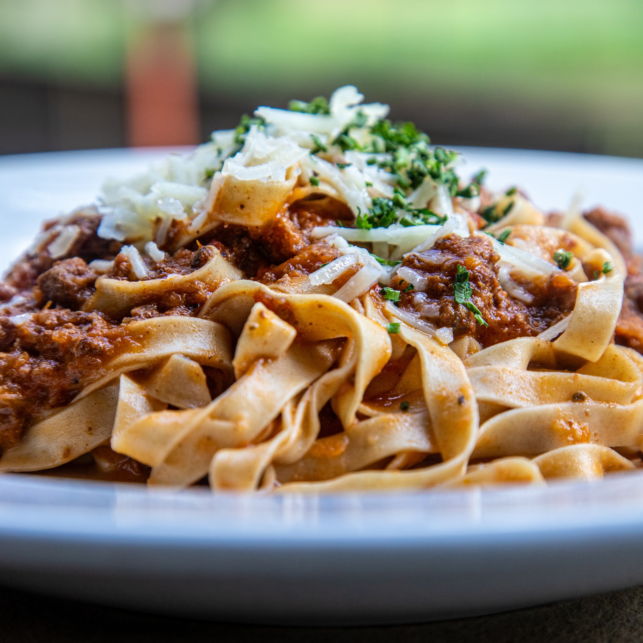 Pasta with meat sauce, grated cheese, and green herbs.