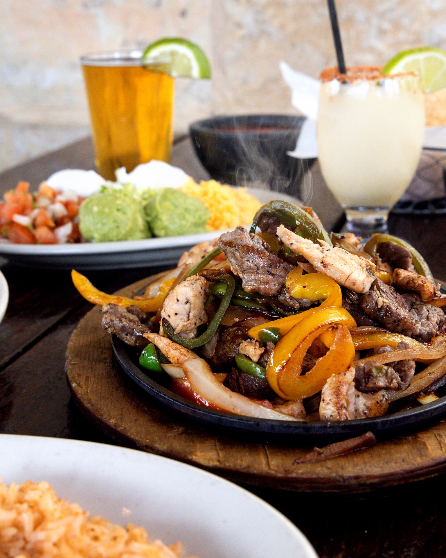 Sizzling chicken and steak fajitas with beer, margarita, and sides.