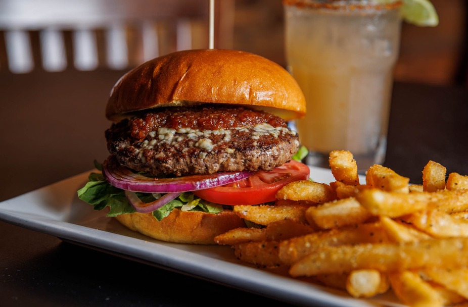 A burger with cheese, sauce, and vegetables, served with fries and a drink.