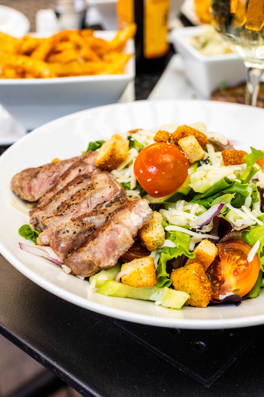 Plate of sliced steak salad with greens, tomatoes, cheese, and croutons.