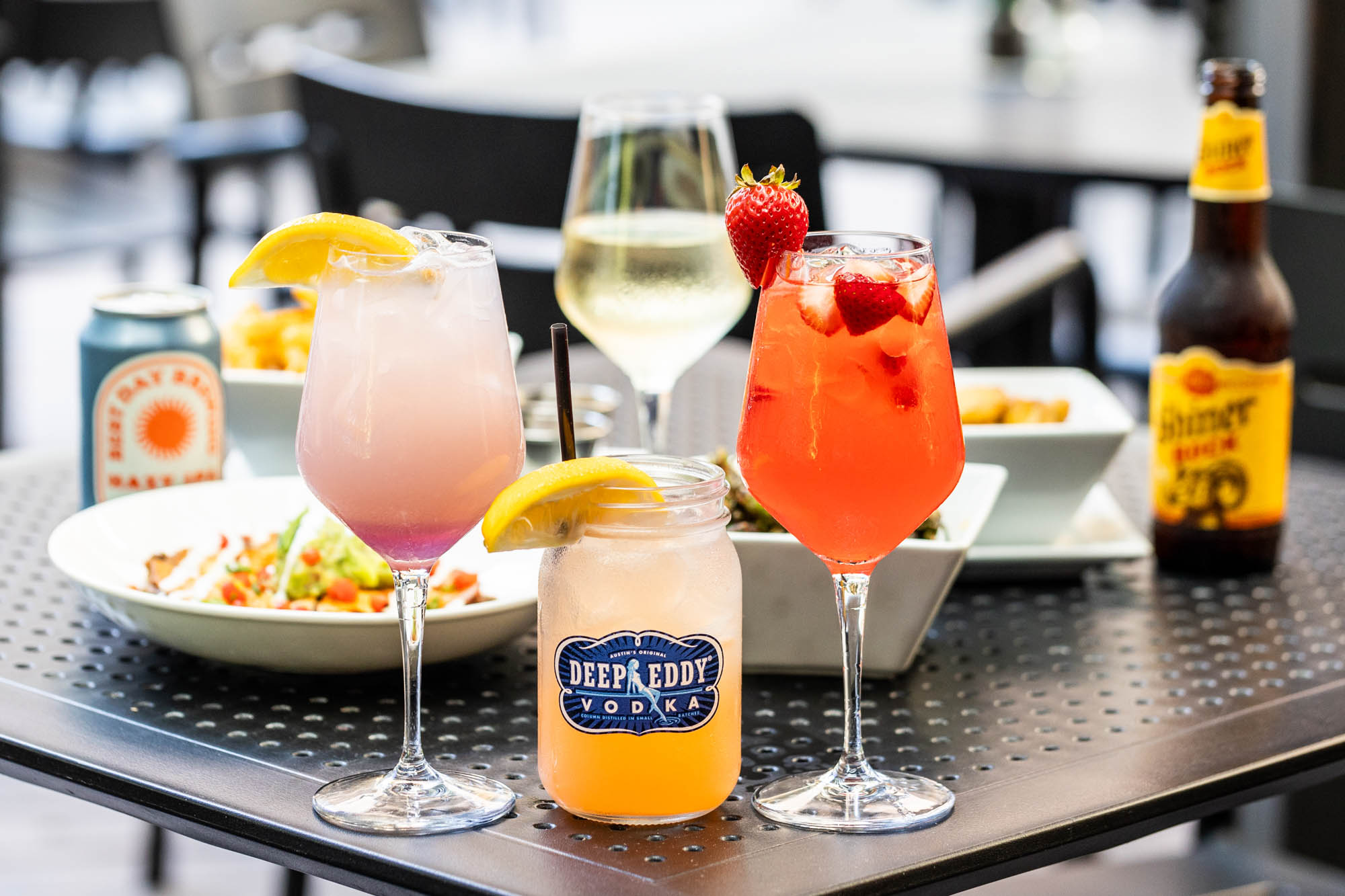 Colorful cocktails, wine, beer, and food on a patio table.