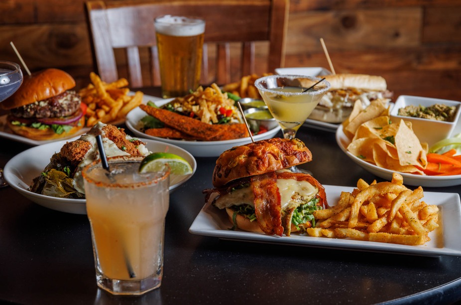 Restaurant table filled with various dishes, including burgers, fries, and cocktails.