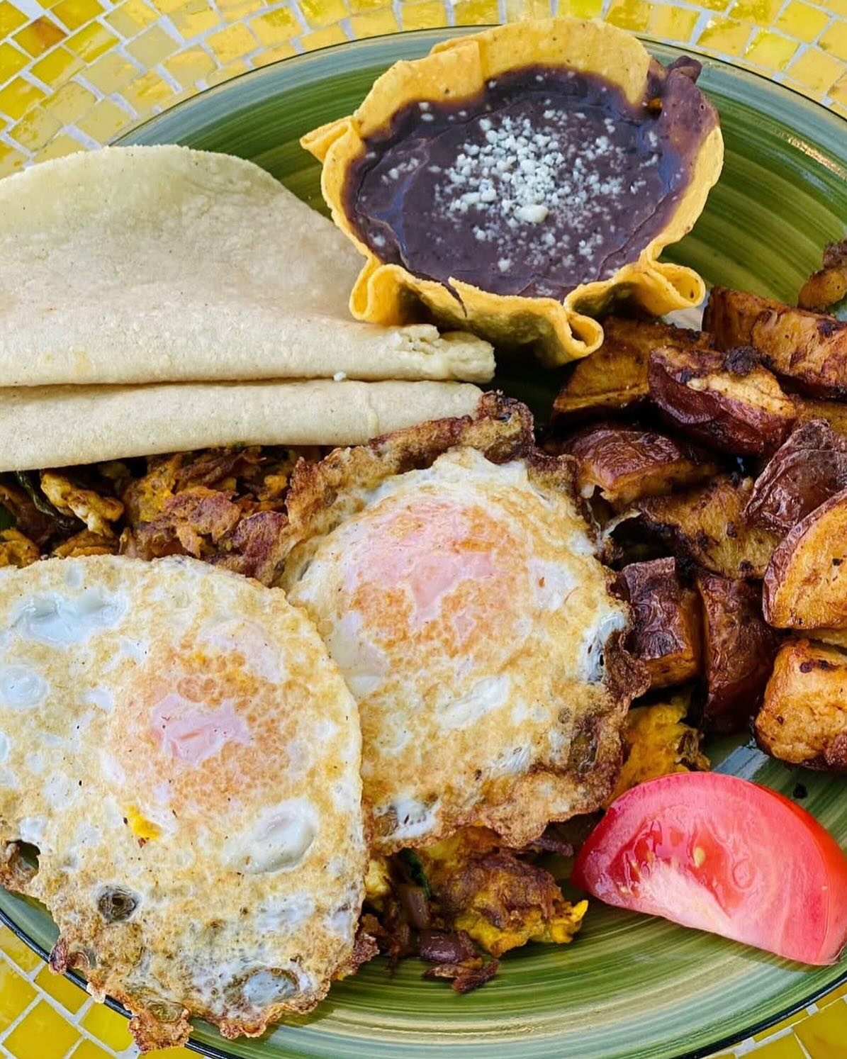 Plate of fried eggs, tortillas, beans, and roasted potatoes with tomato.