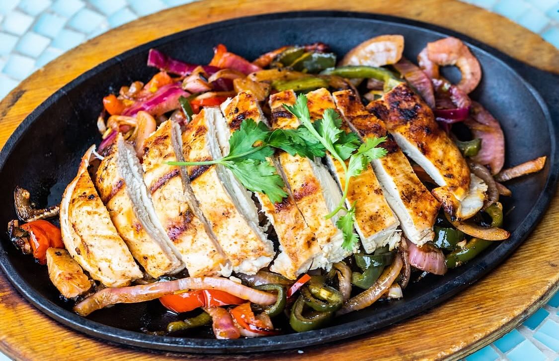Sizzling chicken fajitas with colorful peppers and onions on a skillet.