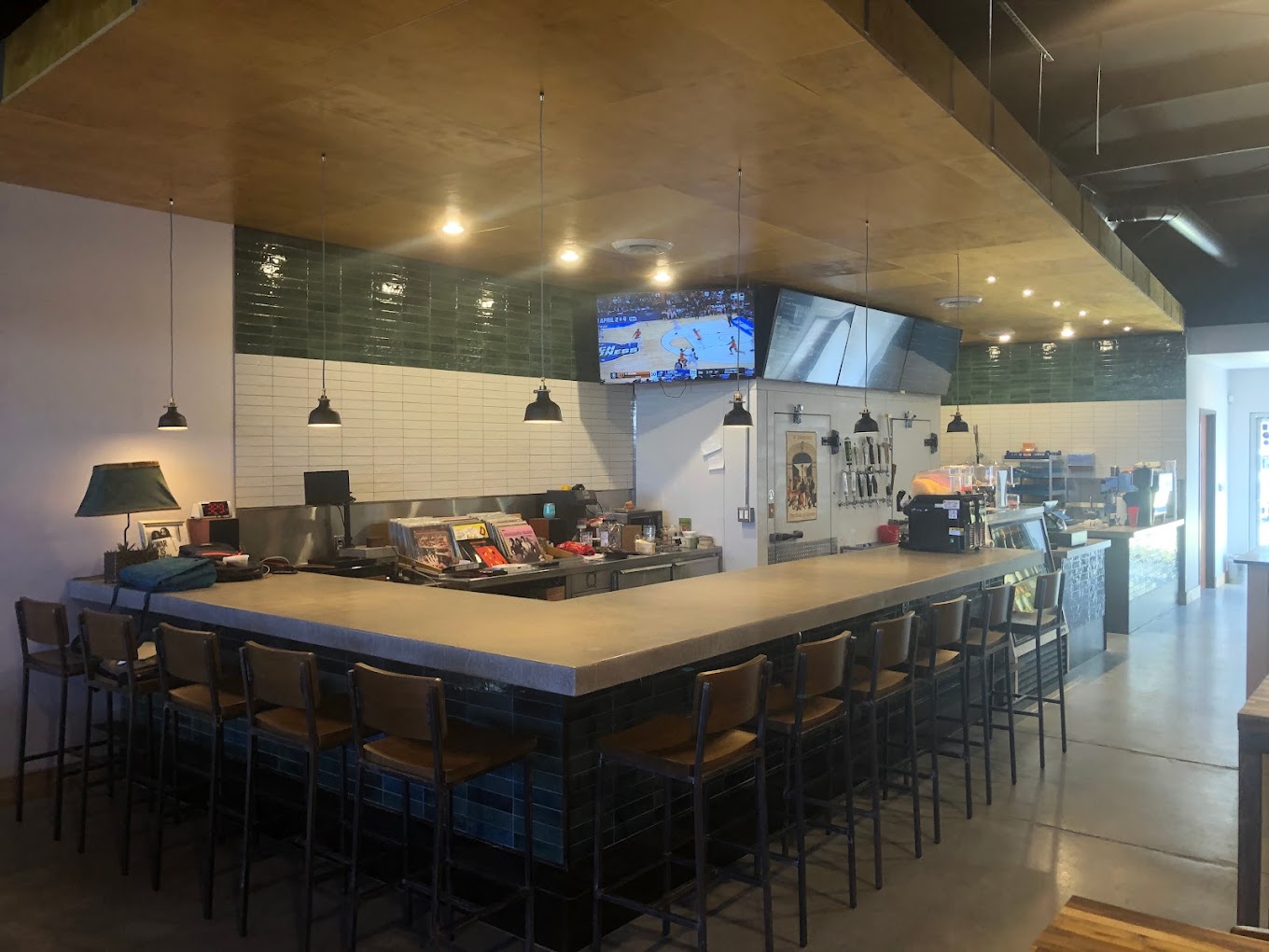 Long bar with empty stools and screens showing a basketball game.