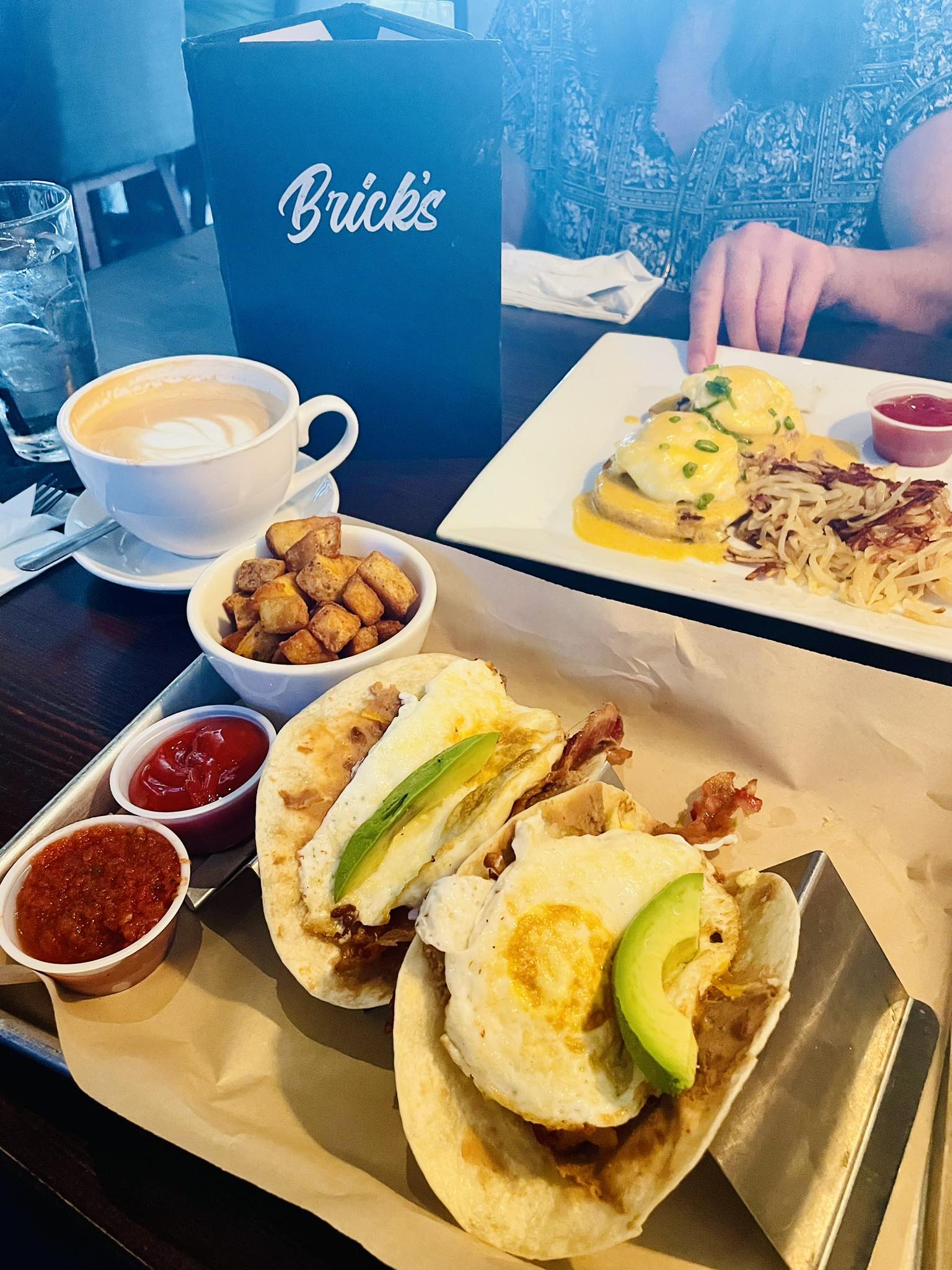 Breakfast meal with egg tacos, Eggs Benedict, potatoes, and coffee.