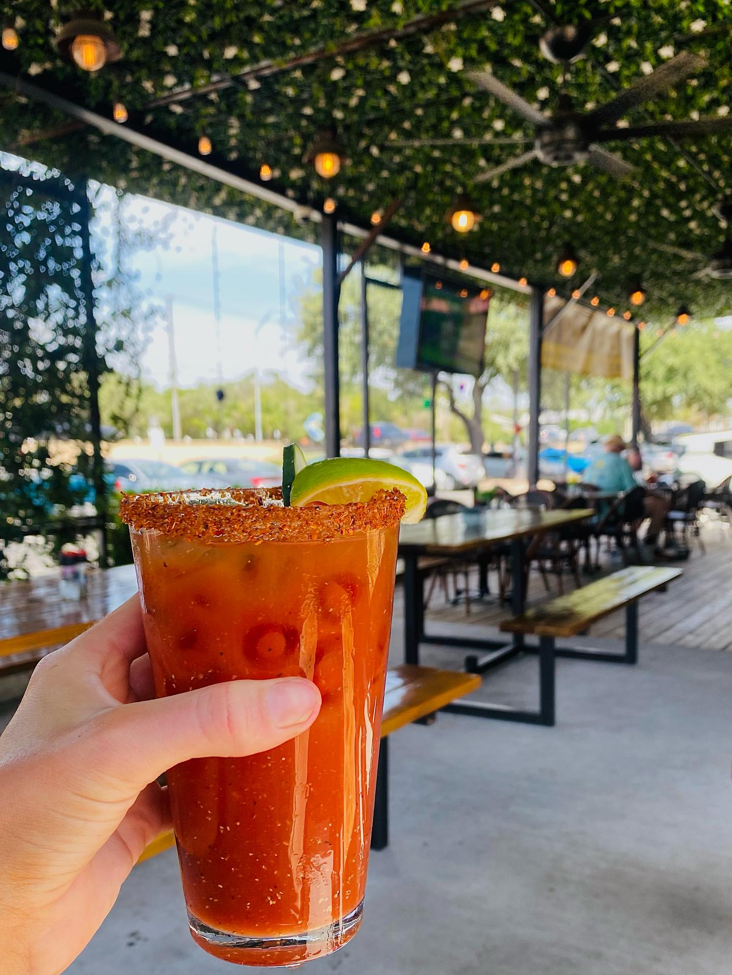 Hand holding a red drink with a lime and chili-salted rim.