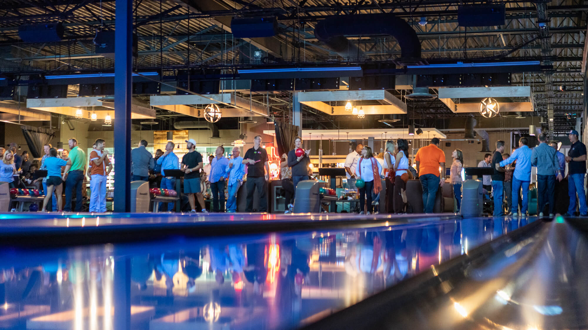 People gathered in a modern bowling alley with reflective lanes.