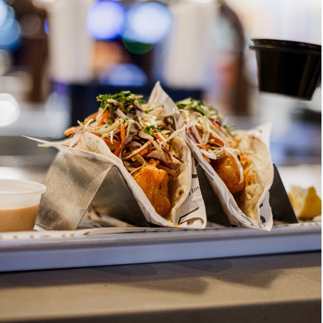 Three tacos with fried filling and coleslaw, on a tray.