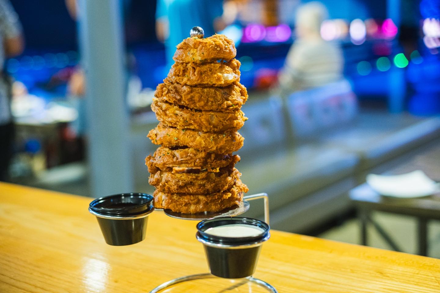 Tall stack of golden-brown onion rings with two dipping sauces.
