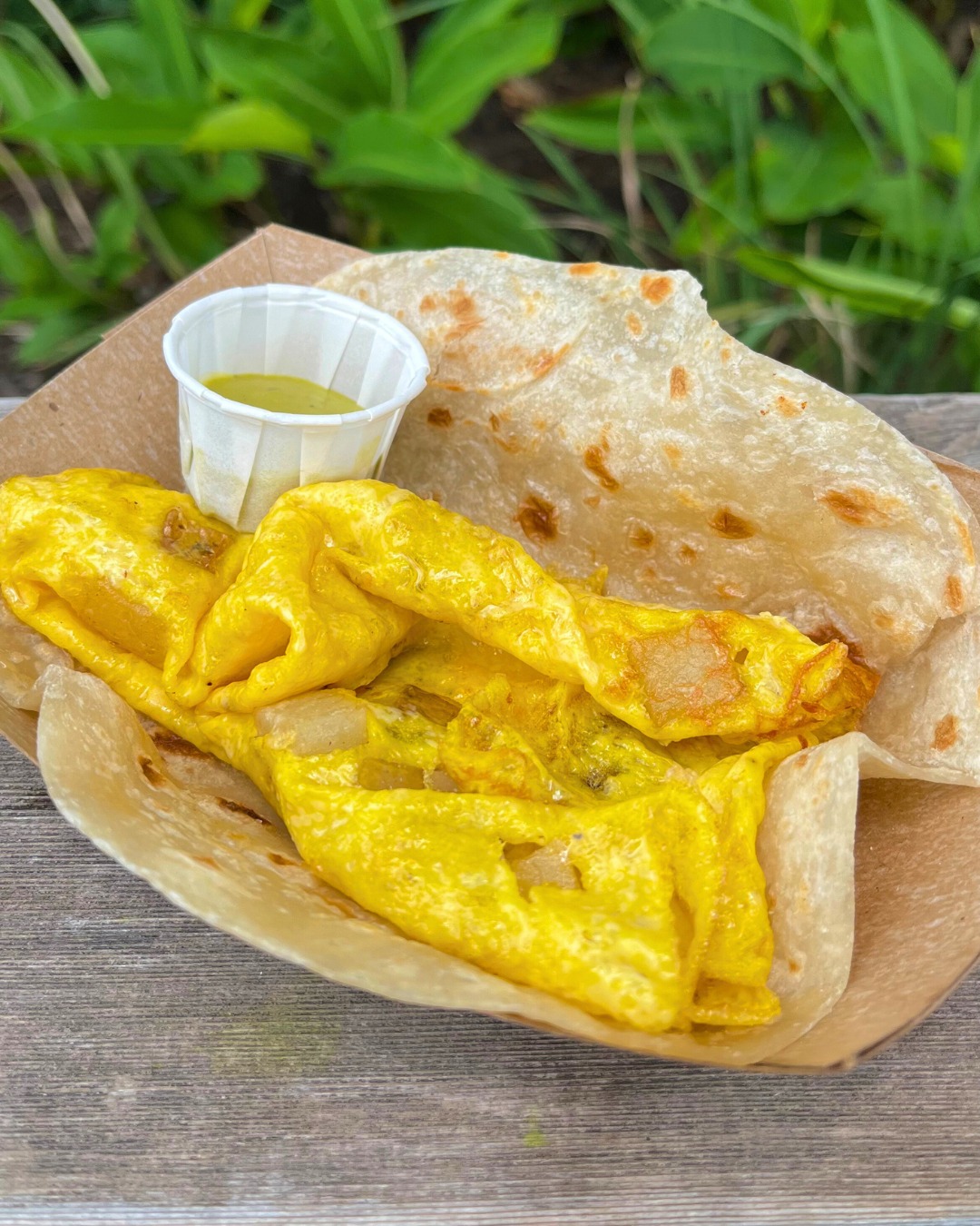 Flatbread with folded yellow omelet and green sauce in a tray.