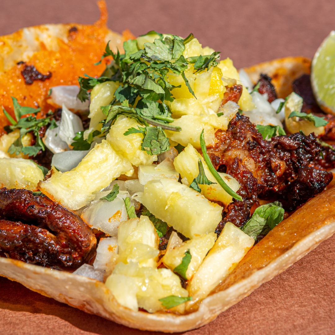 Taco with dark meat, pineapple, diced onions, cilantro, and lime wedge.