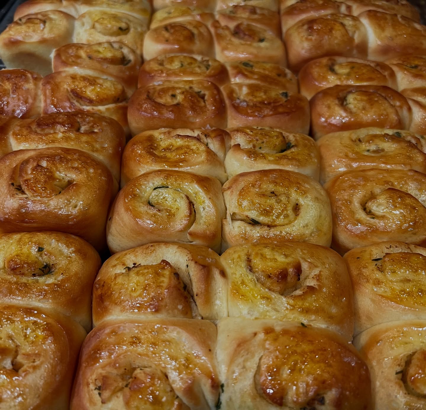 Many golden-brown savory spiral buns with visible green and yellow fillings.