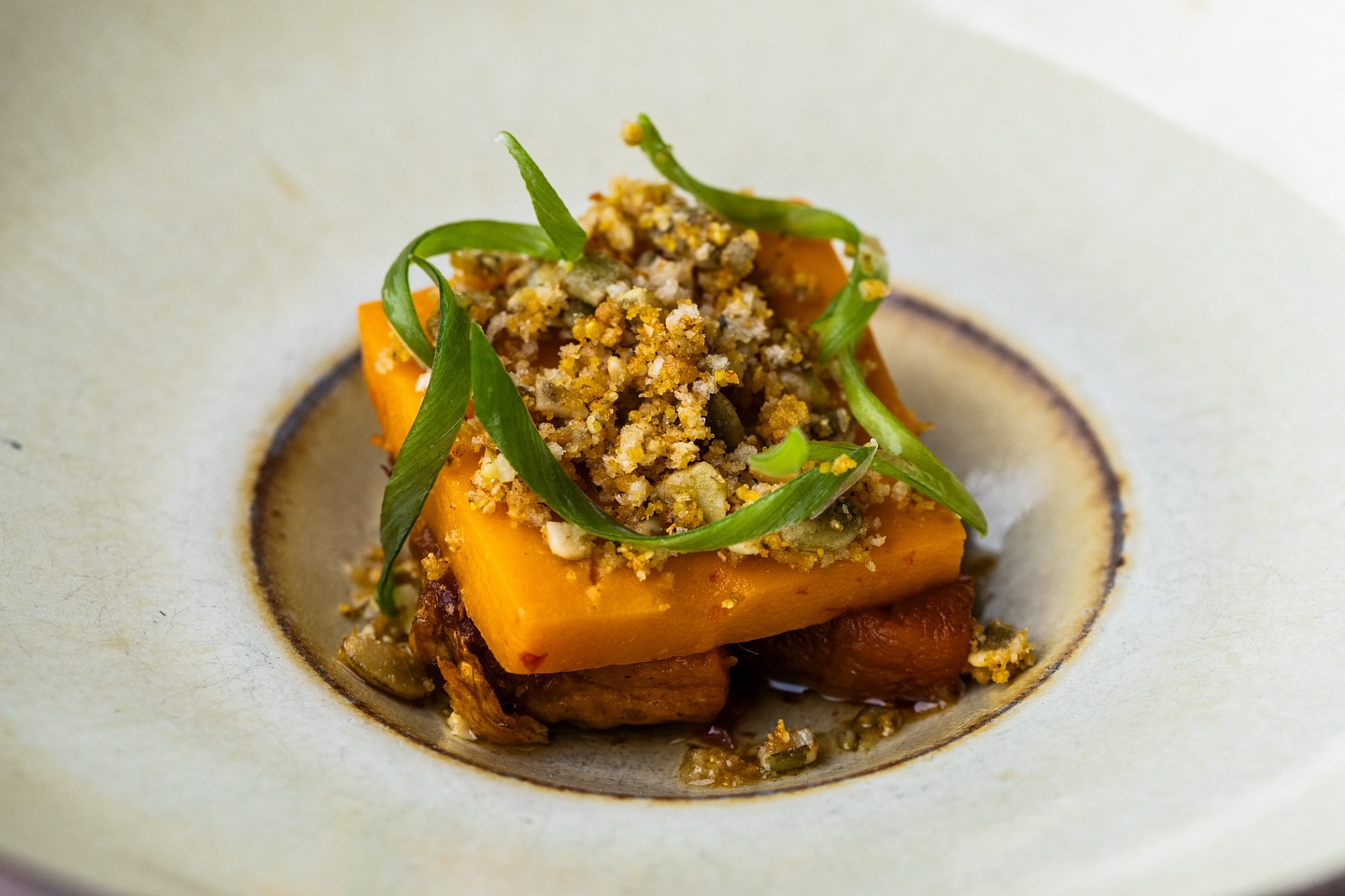 Orange vegetable pieces with crumb topping and green garnish.