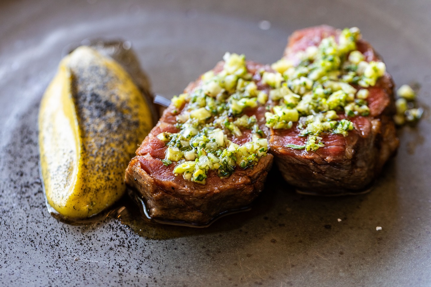 Cooked steak with green relish and yellow puree on a plate.
