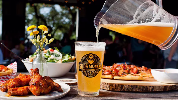 Suds Monkey beer poured with chicken wings, flatbread, and salad.