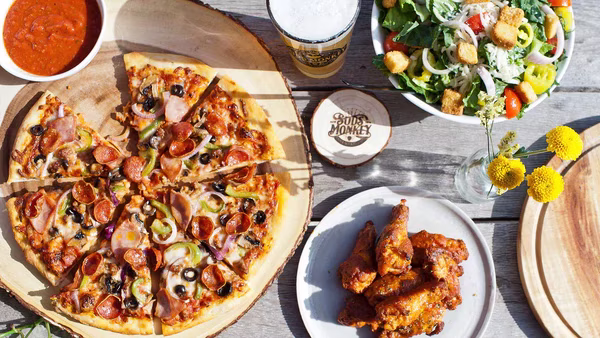 Pizza, wings, salad, and beer on a wooden outdoor table.