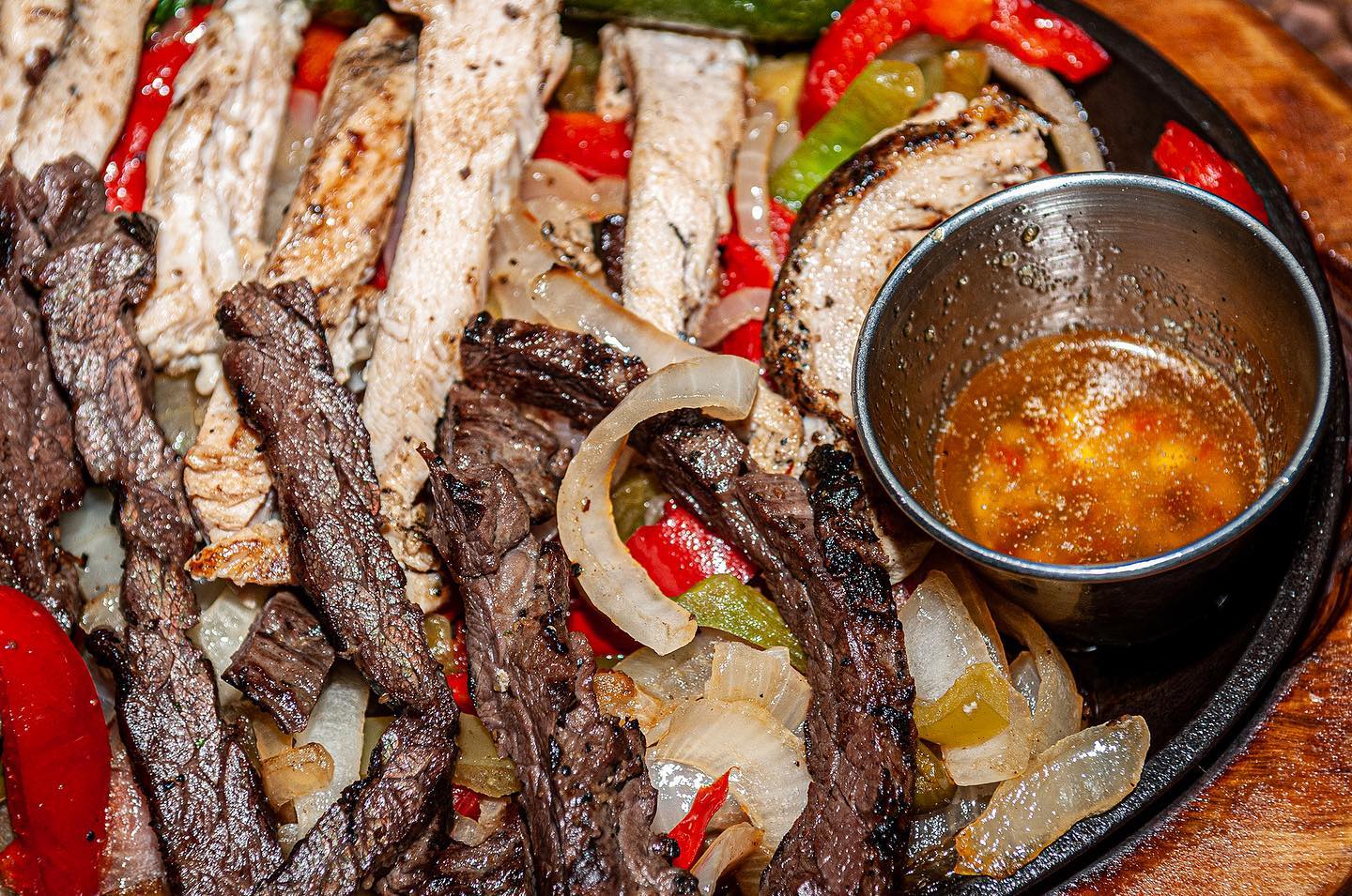 Sizzling beef and chicken fajitas with peppers, onions, and sauce.