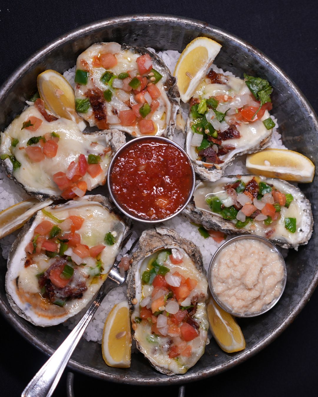 Baked oysters topped with melted cheese, salsa, lemon, and sauces.