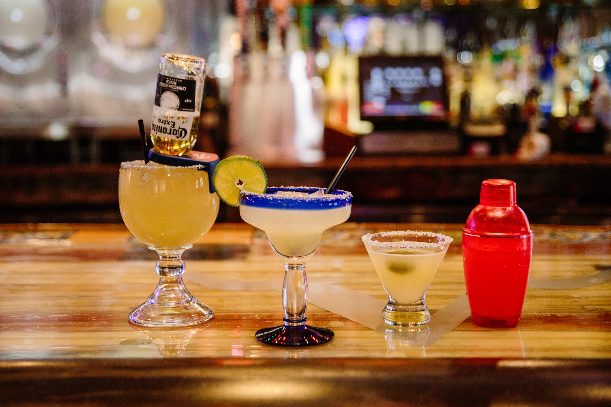 Two margaritas, martini, and shaker on a bar counter.