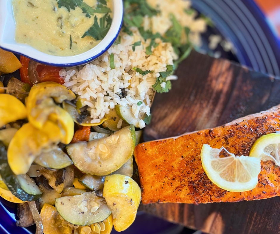Cooked salmon, roasted vegetables, rice, and creamy sauce on plate.