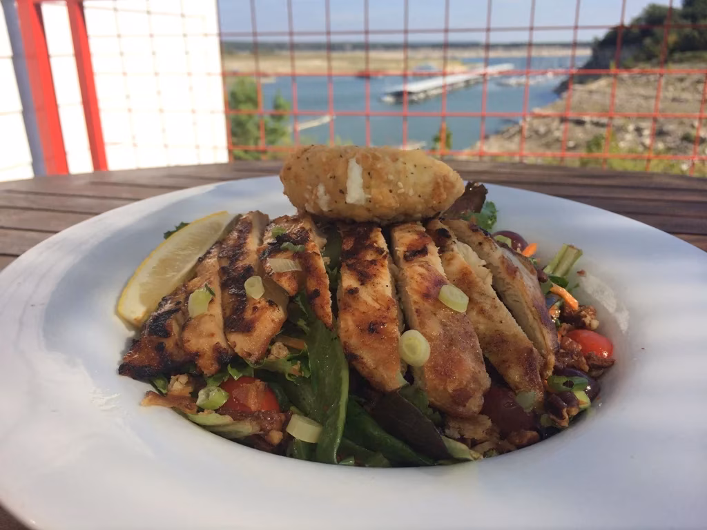 Grilled chicken salad with a lemon wedge and lake view.