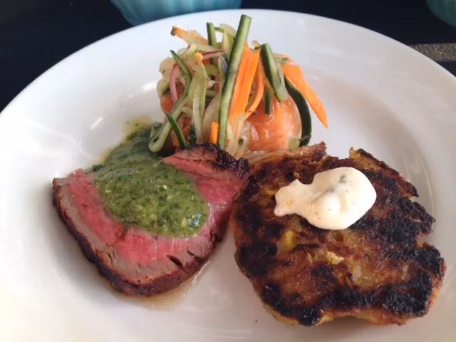 Sliced beef with green sauce, fried potato, and shredded vegetable salad.