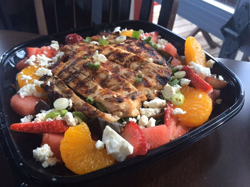 Grilled chicken salad with fruit, crumbled cheese, and green onions.