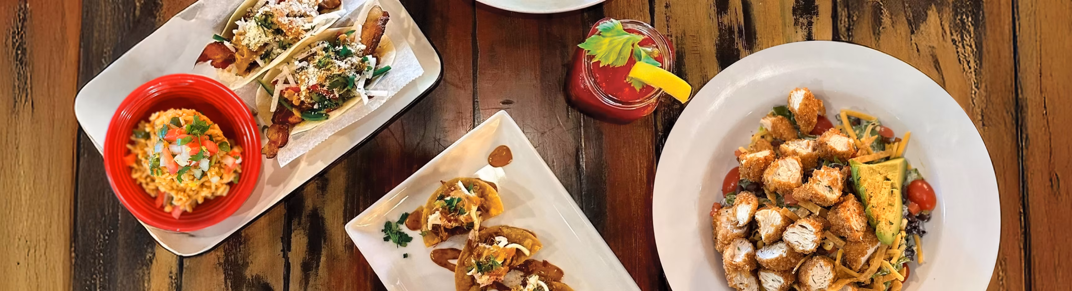 Tacos, rice, chicken salad, and a red drink on a wooden table.