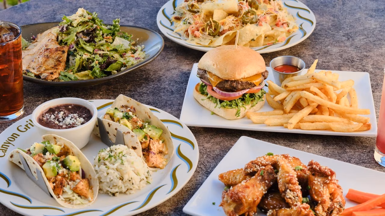 Plates of tacos, burger, fries, nachos, wings, and salad on table.