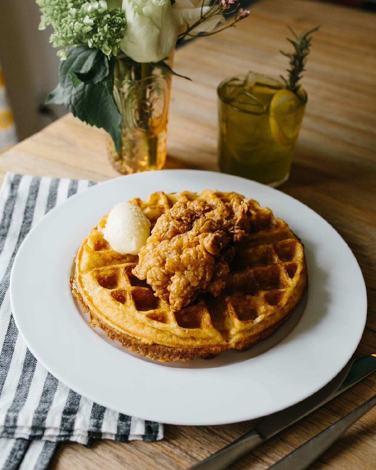 Fried chicken and waffles with butter, beverage, and flowers.