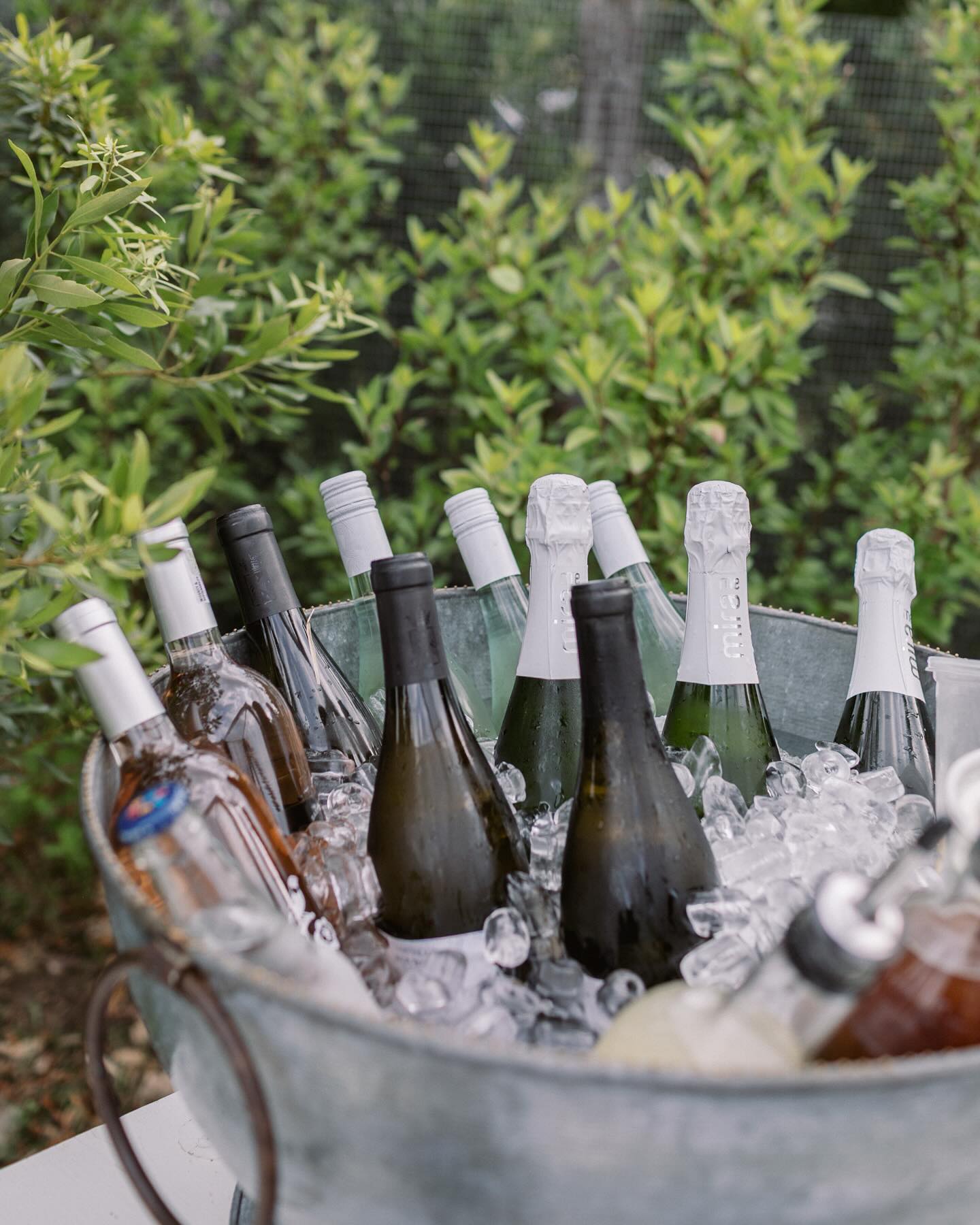 Assorted bottles of wine and drinks chilling in an ice bucket outdoors.