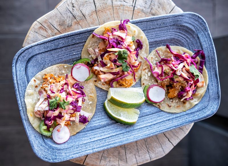 Three tacos topped with purple cabbage, radish, and lime wedges.