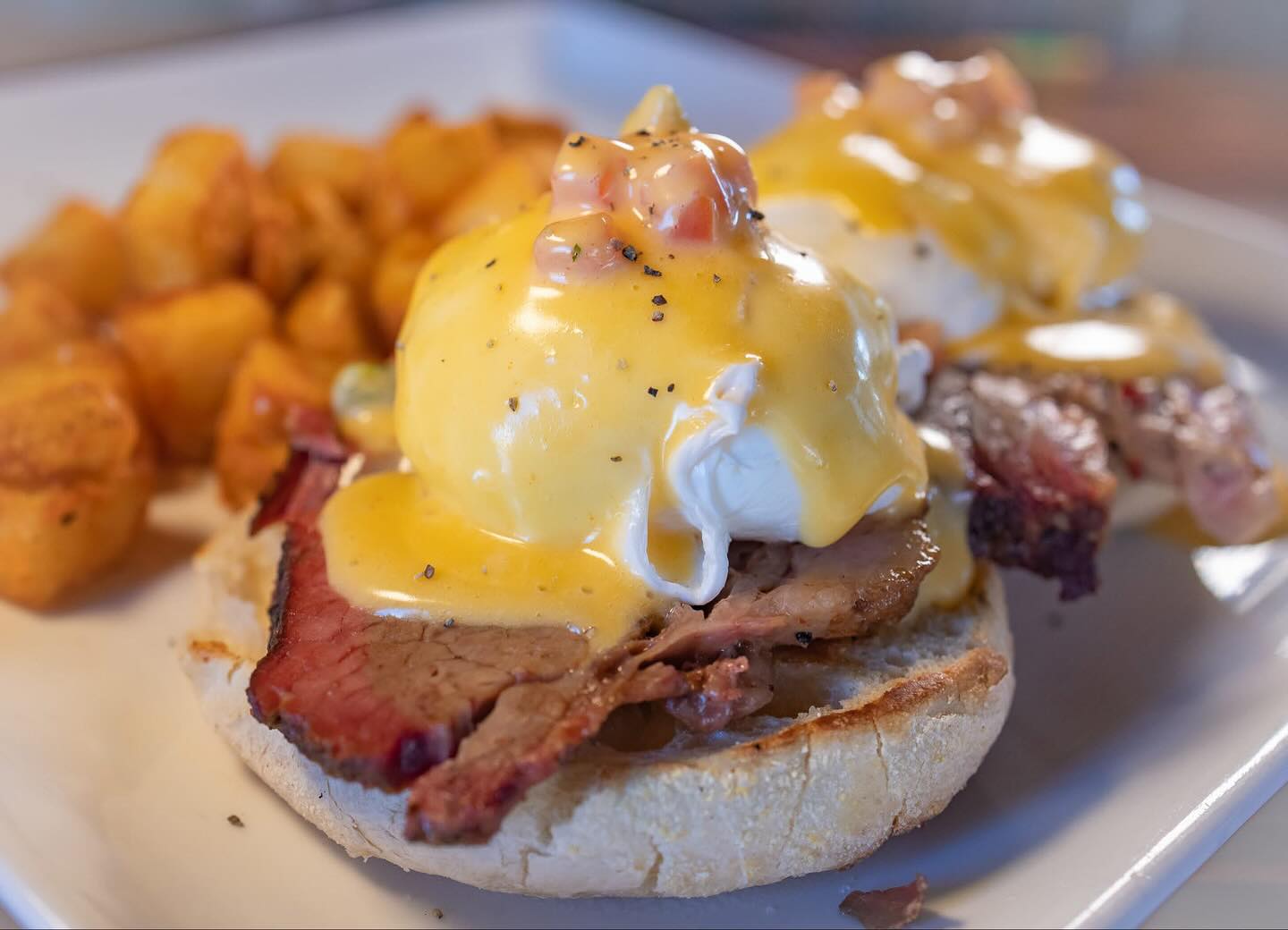 Eggs Benedict with sliced meat, hollandaise, poached eggs, and home fries.