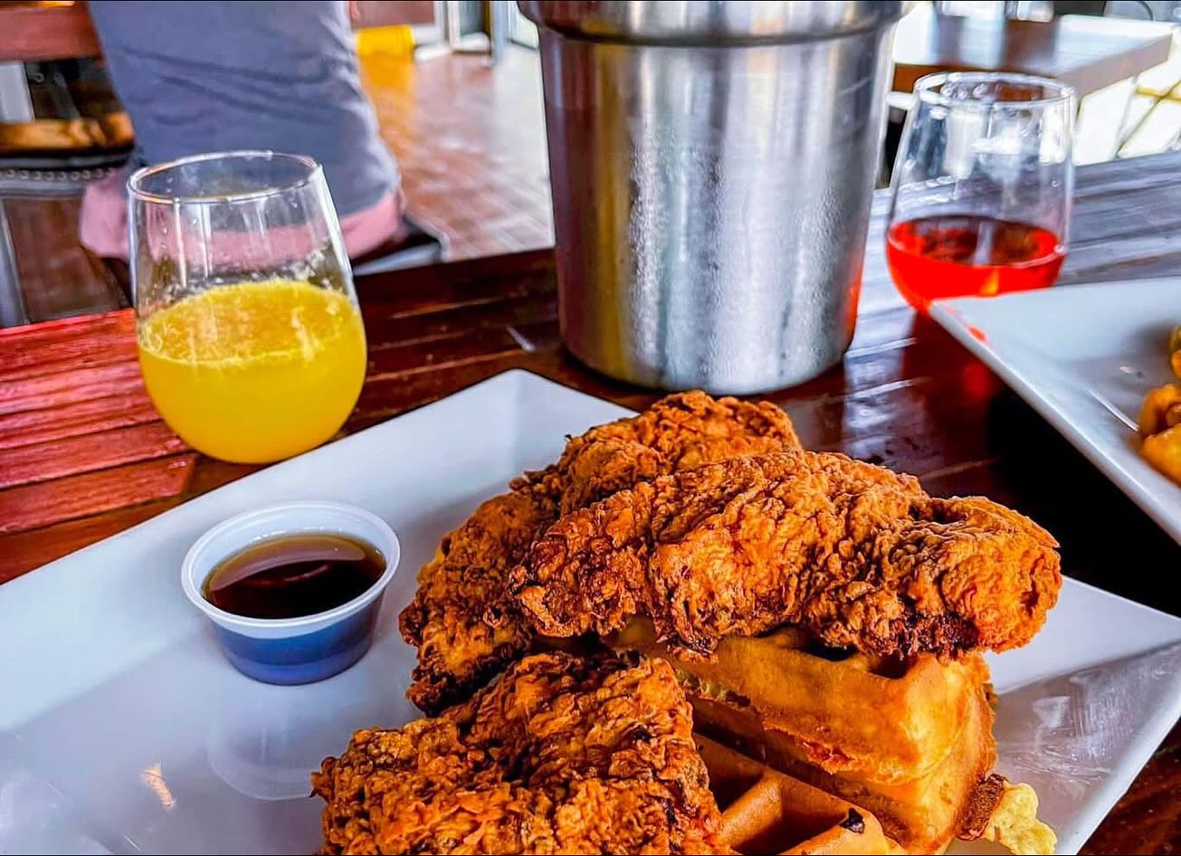 Plate of chicken and waffles with syrup and a glass of orange juice.
