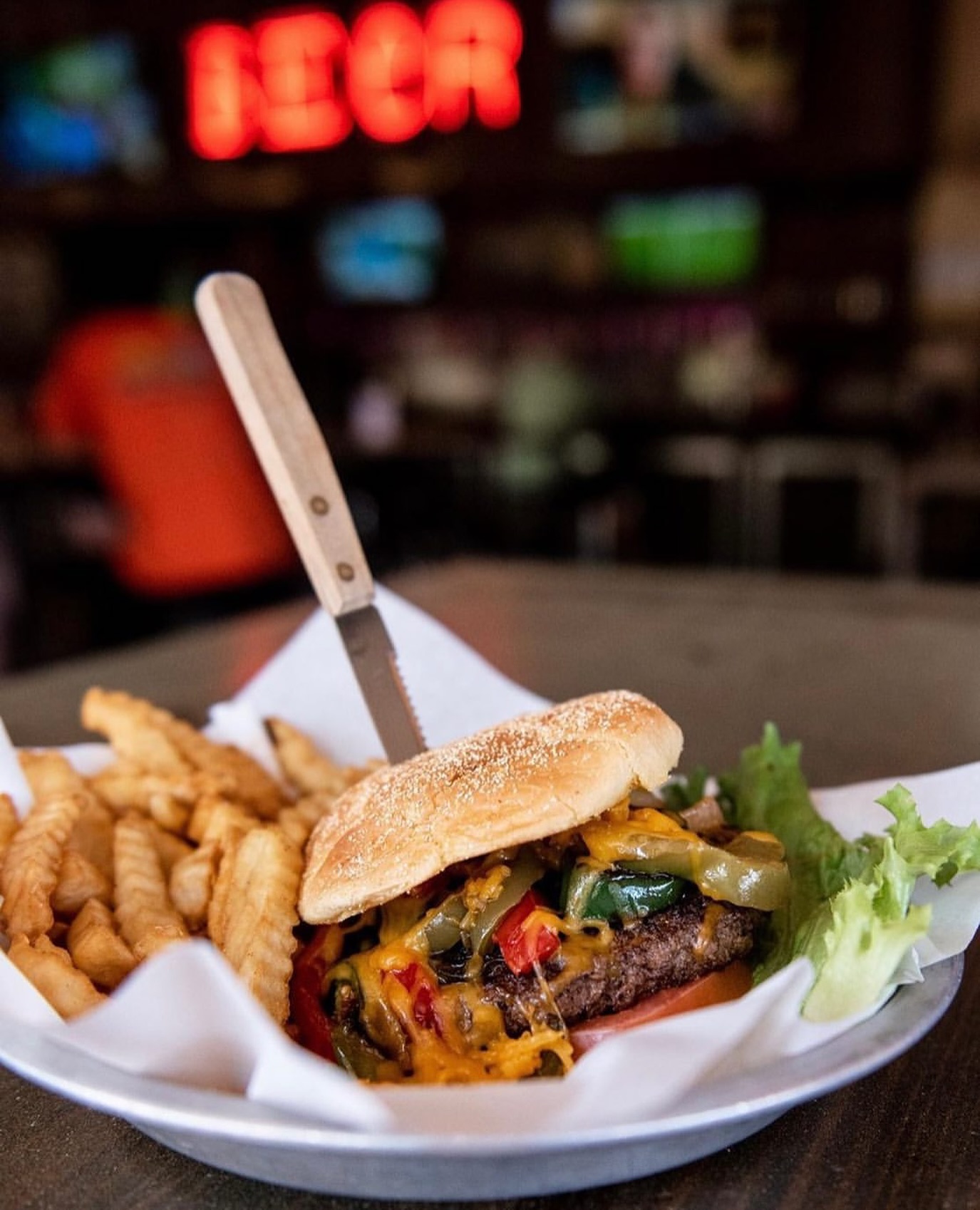 Plate of burger, fries, and knife, with red BEER sign.