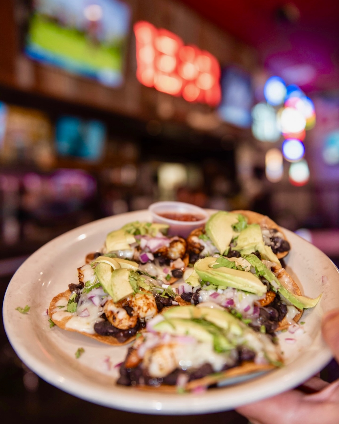 Shrimp tostadas topped with black beans, avocado, cheese, and red onion.