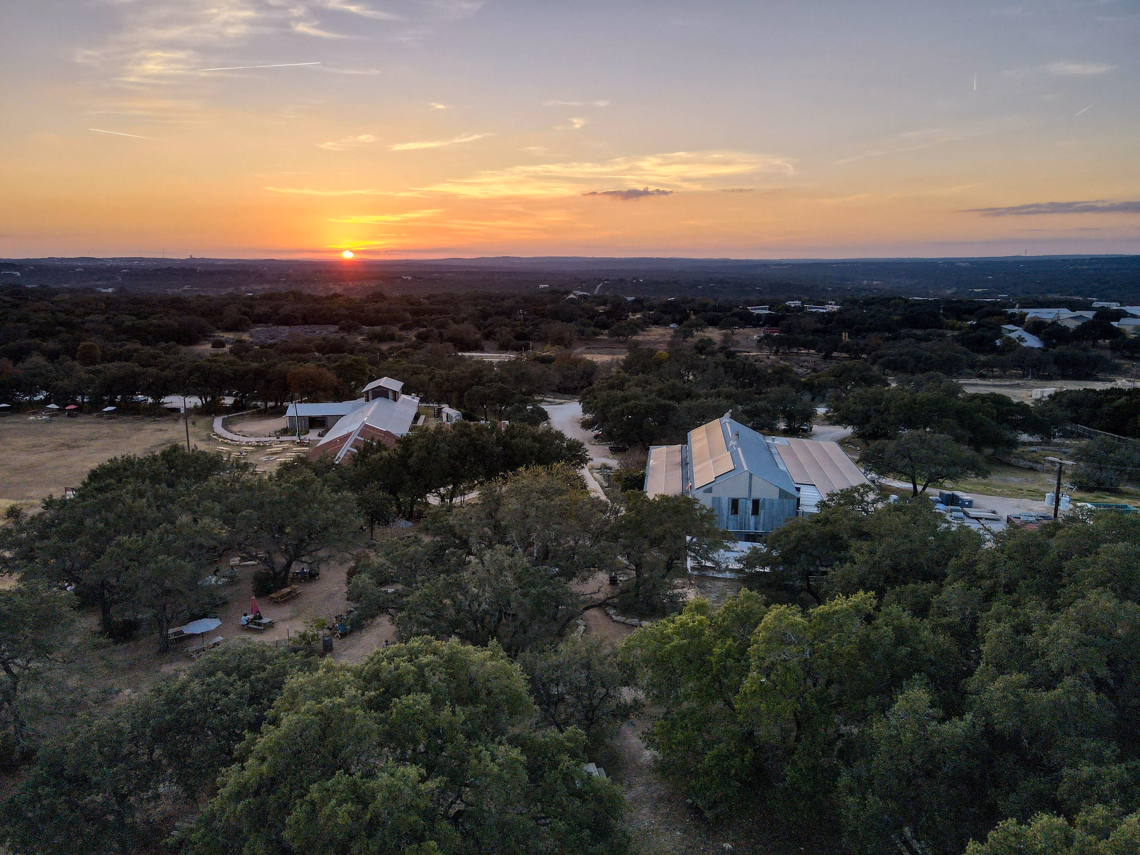 Sunset over buildings with solar panels, surrounded by trees.