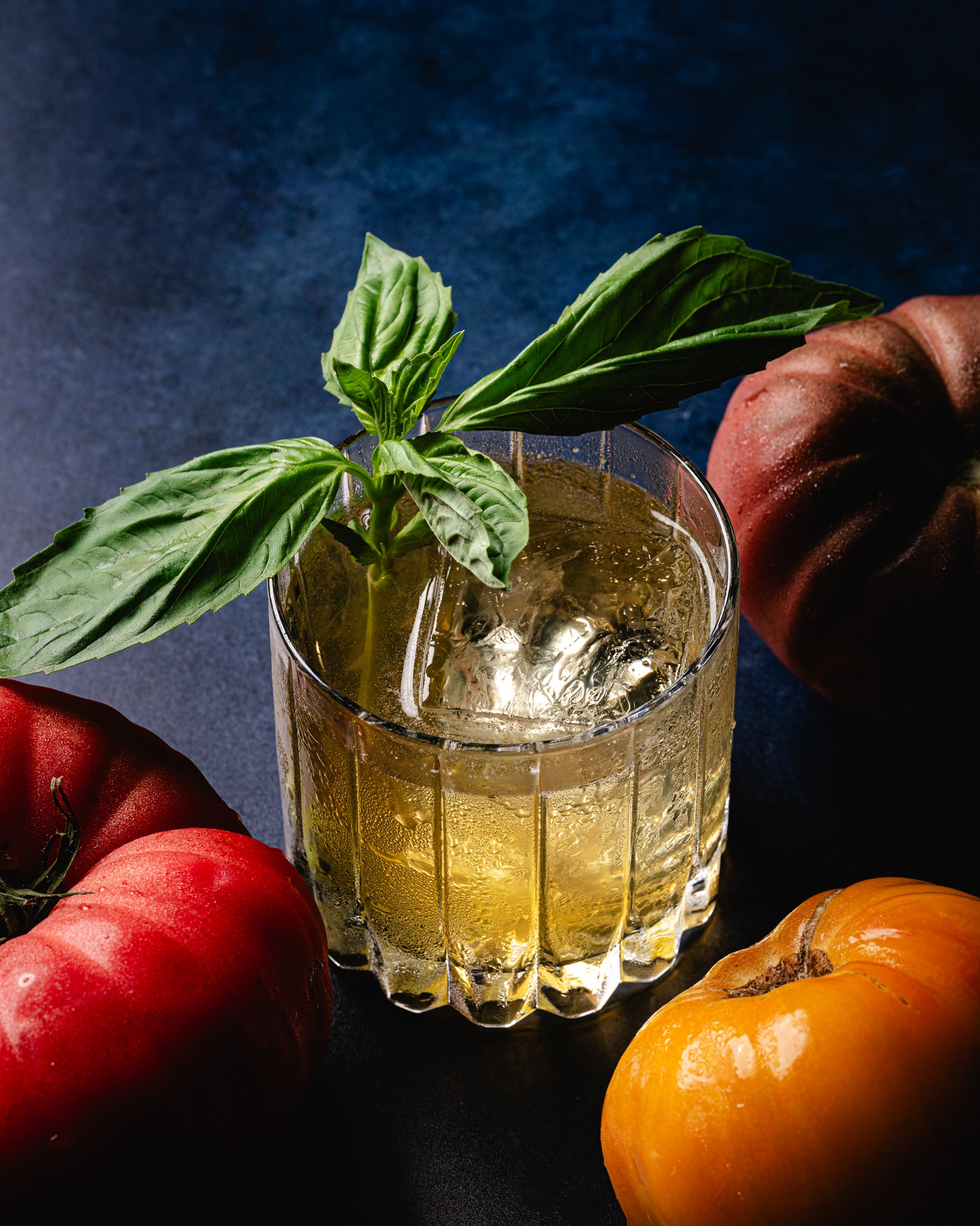 Glass of iced drink with basil and three colorful tomatoes.