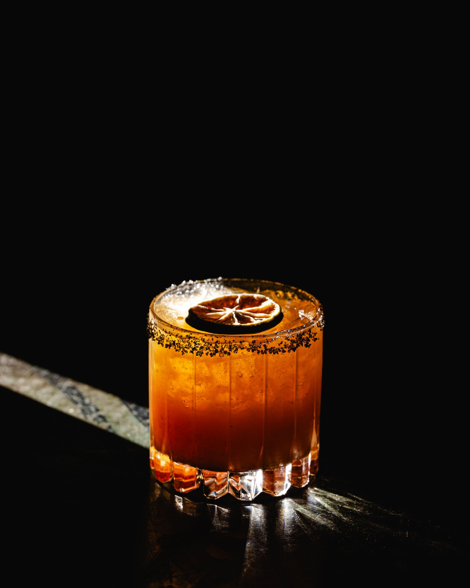 Amber drink in glass with dried lime and dark rim.