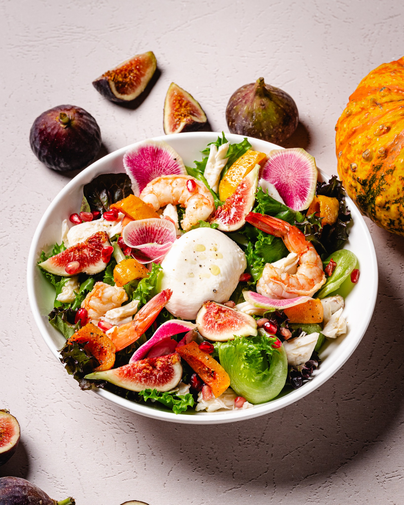 Salad with shrimp, burrata, figs, radishes, and pomegranate on light background.