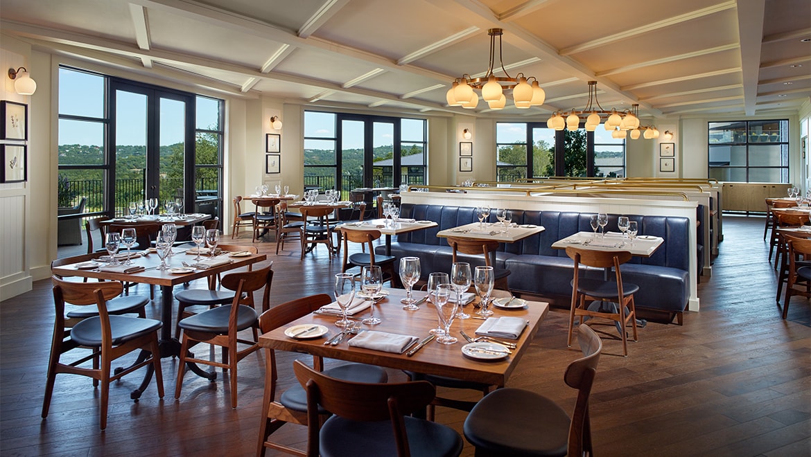 Dining room set with tables, blue booths, and windows overlooking nature.