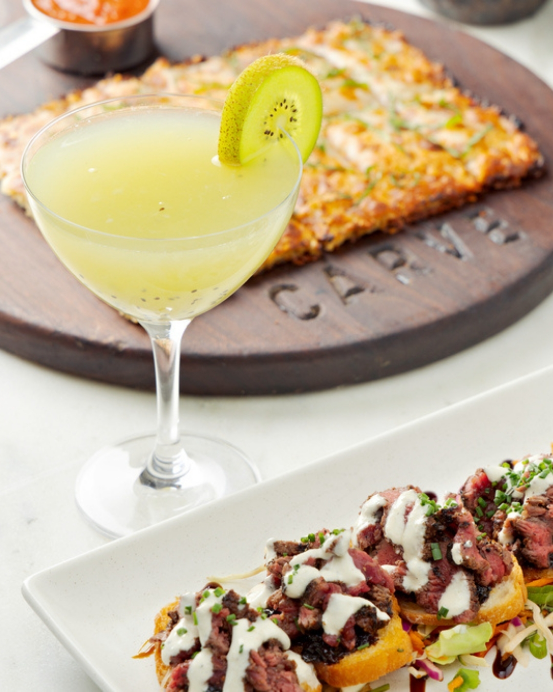 Kiwi drink, flatbread on wood, and meat toasts with sauce.