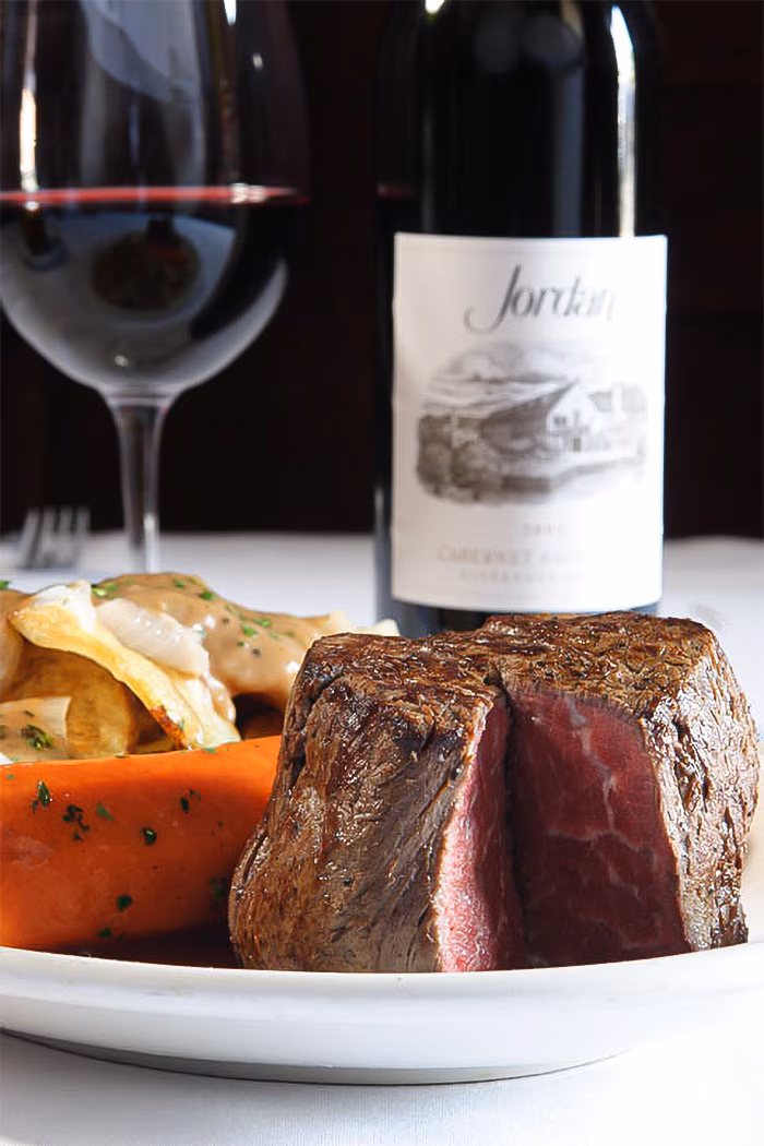 Medium-rare steak with vegetables, red wine glass, and wine bottle.