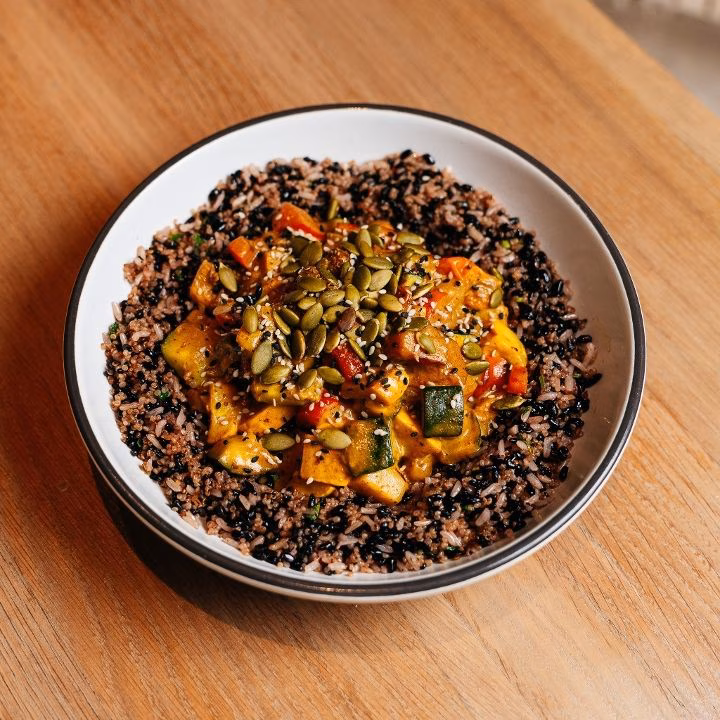 A bowl of wild rice topped with vegetable curry and pumpkin seeds.