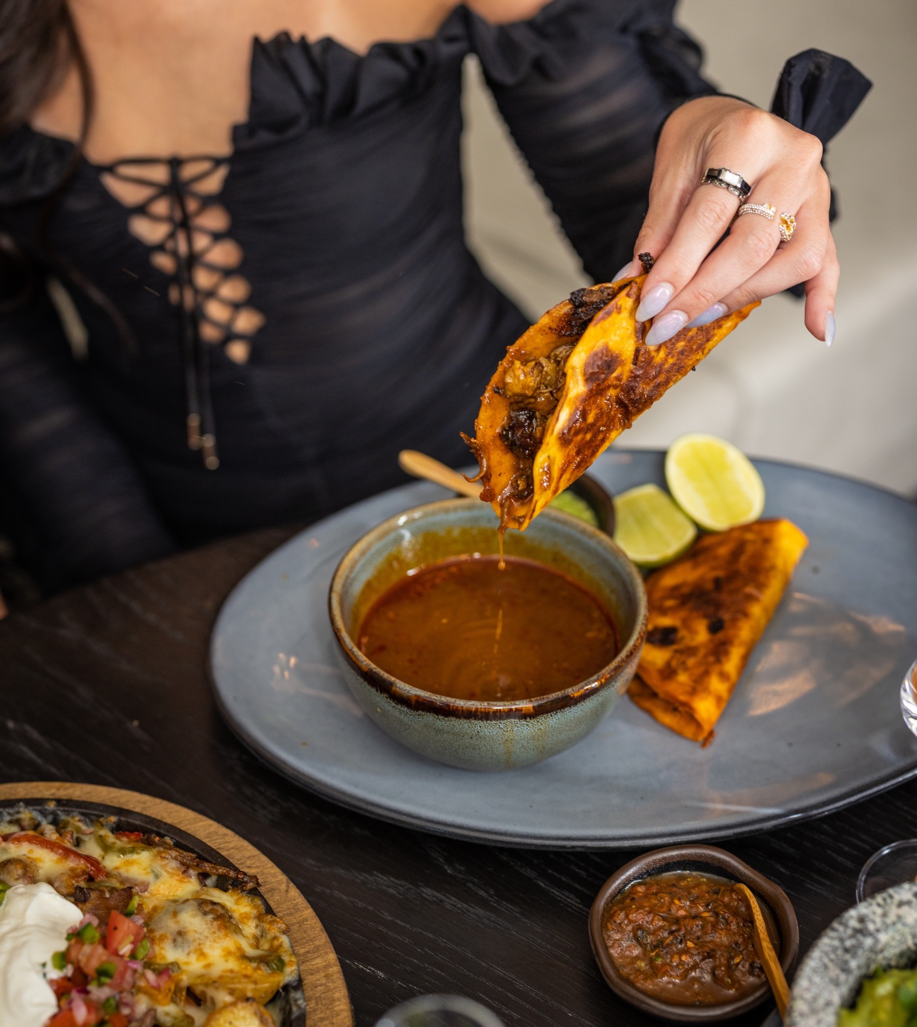 Hand holds a taco dripping into a bowl of red broth.